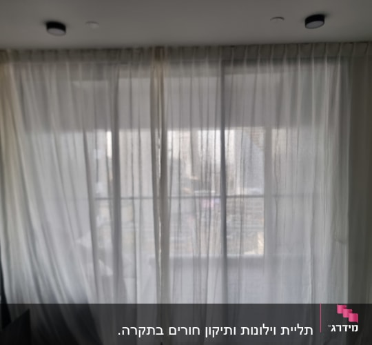 וילון לבן תלוי על חלון בחדר